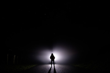 Silhouette of a woman in the darkness. Night Photography. Bright light shining behind dark mysterious figure. Ghostly, mystical, surreal person standing.