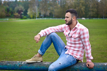 Young handsome guy Cowboy. male farmer is sitting on his fence on his ranch. Rural landscapes, countryside. Trees, field, farm. Stock photos for design