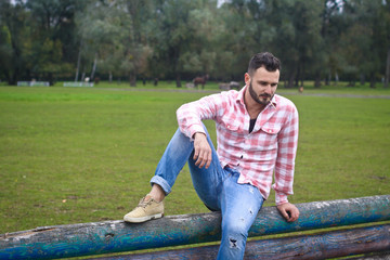 Young handsome guy Cowboy. male farmer is sitting on his fence on his ranch. Rural landscapes, countryside. Trees, field, farm. Stock photos for design