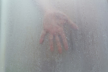 hand through a shower screen with drops on a light background