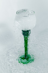 Fototapeta na wymiar wine glass with a green leg with splashes of water on a white background