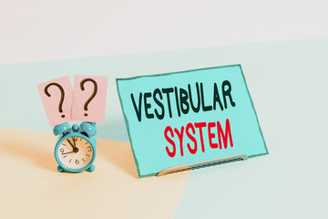 Writing note showing Vestibular System. Business concept for provides the leading contribution to the sense of balance Alarm clock beside a Paper sheet placed on pastel backdrop