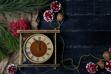 Brown and golden vintage clock, pine branches and red painted cones on black background. Merry...