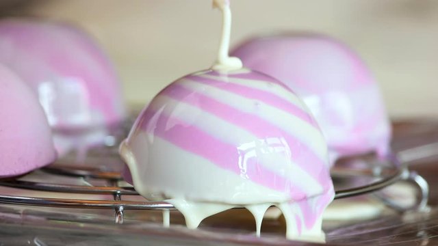 Glazing of french mousse cake close up. Purple icing on the hemispherical cakes. Cooking yummy dessert at french cafe.
