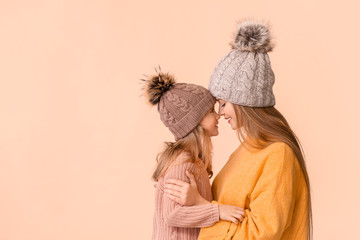 Woman and her little daughter in winter clothes on color background