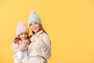 Woman and her little daughter in winter clothes on color background