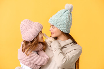 Woman and her little daughter in winter clothes on color background