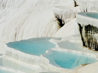 Natural spring water in white travertine terrace formations, covered by carbonate mineral, turns into powder blue color under sunlight. Travel destination in Pamukkale, Cotton Castle in Turkey. 