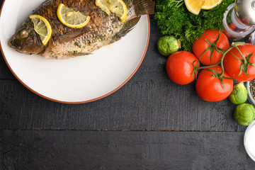Oriental or European cuisine, cooked fish with lemon on a black wooden background, with vegetables and ingredients. Flat lay with space for an inscription or dizan