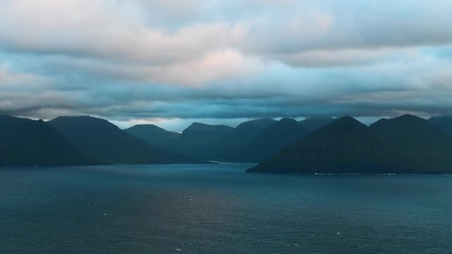 Evening timelapse with moving clouds and blue mountain peaks in the summer Faroe Islands, Denmark. UHD 4k video