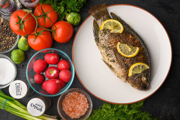 Cooked fish with lemon, on a black wooden background, with ingredients and vegetables. Delicious and healthy food.