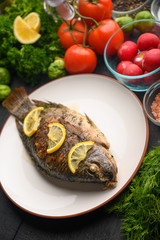 Cooked fish with ingredients, on black background. Vertical frame.