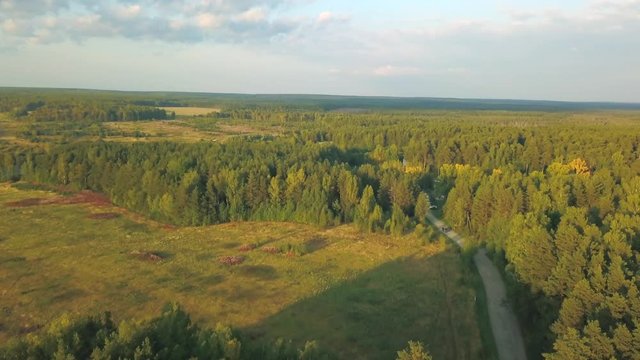 Aerial view of large green fields, forests and road at the sunset against blue cloudy sky in summer or in the beggining of the autumn. Stock footage. Beautiful countryside views