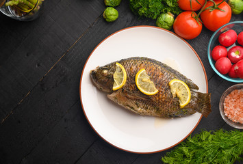 Oriental or European cuisine, cooked fish with lemon on a black wooden background, with vegetables and ingredients. Flat lay with space for an inscription or dizan