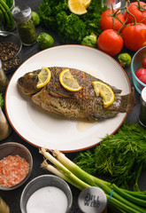 Cooked fish with ingredients, on black background. Vertical frame.