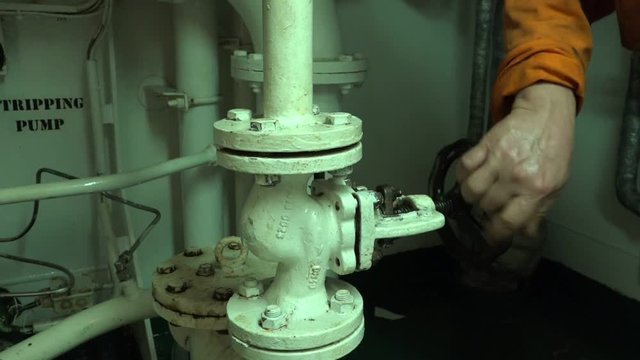 crew member hand turns on pipeline big black safety valve near stripping pump in oil tanker engine compartment close view
