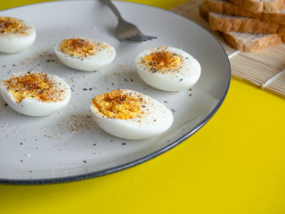 ฺBoiled egg topped with Cayenne pepper Pepper and Salt on a white dish,Egg colors white and yellow,Eat with bread