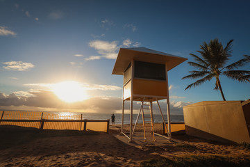 Lifeguard hut on the beach at sunrise with silhouette of a man watching the ocean