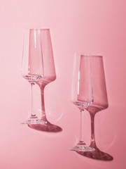 Two empty champagne glasses on a pink background in the harsh light.