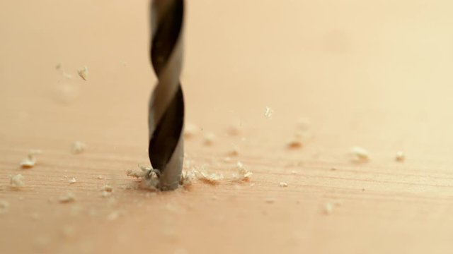 SLOW MOTION, MACRO, DOF: Wood chippings and sawdust flies off a metal bit drilling into a plank. Detailed shot of a sharp metal drill boring a hole into a wooden board. Handyman drilling holes in wood