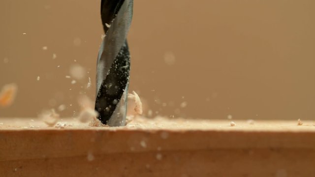 SLOW MOTION, MACRO, DOF: Wood chippings fly off the plank sitting on a carpenter's workbench as handyman drills holes into the workpiece. Sawdust flies off spinning drill boring a hole into a board.