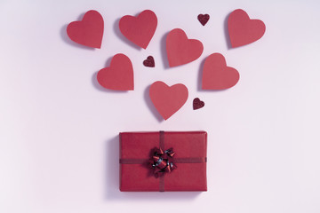 Valentine's day composition. Burgundy hearts blowing from gift box on pastel pink background. Love...
