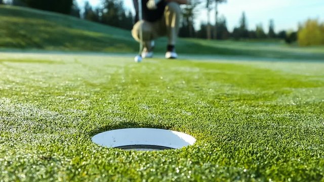 Golfer on putting green narrowly misses the cup, ending in frustration