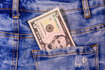 American five dollar banknote in a pocket of blue jeans