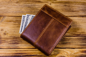 Brown leather wallet and one hundred dollar banknotes on the wooden background