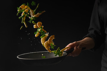 Thai cuisine, the chef cooks shrimps with lemon, frying in a pan. Freezing in motion, on a black background. Advertising photo, seafood sale.