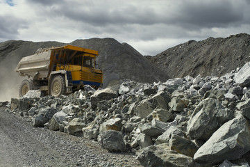 Heavy mining dump truck in a limestone quarry with huge fragments of rock in the foreground. Quarry equipment. Mining industry.