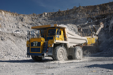 Heavy quarry dump truck transports stone ore inside a large quarry, close-up.