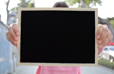 Woman with hand holding showing black chalkboard outdoor blurred background, frame composition with copy space for banner design or card and online shopping marketing or school project