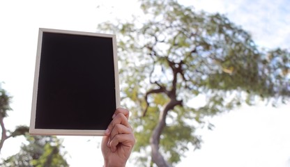 Woman with hand holding showing black chalkboard outdoor blurred background, frame composition with copy space for banner design or card and online shopping marketing or school project