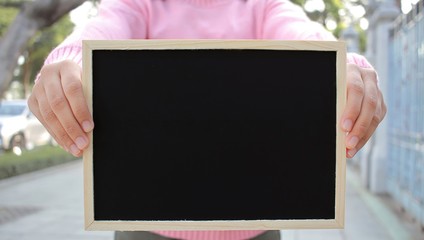 Woman with hand holding showing black chalkboard outdoor blurred background, frame composition with copy space for banner design or card and online shopping marketing or school project