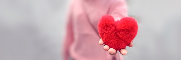 Red heart in hand, Valentine background composition, sending love, shearing kindness, best wishes to people, romantic and unconditional love, pastel pink color with blurred background