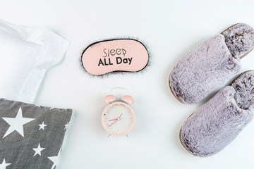 Flat lay with Soft fluffy slippers gray color, pillow, blindfold and pink alarm clock isolated on white background. top view, overhead, mockup, template. Time for rest