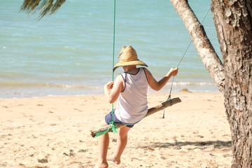 Boy sitting on a log swing on a tropical beach in North Queensland
