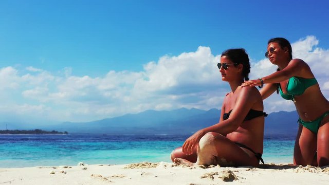 Bali, Indonesia, young female homosexual couple sunbathing on the beach. Girl cleaning sand from her girlfriends back