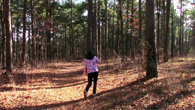 A woman walks on a forest trail, filming a video with her phone