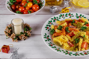 Fototapeta na wymiar Christmas dinner. Tricolor rotini pasta with cherry tomato and candle.