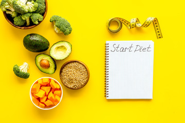 Diet program mockup. Start diet text in notebook near vegetables on yellow background top view