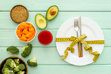Diet concept. Fork and knife tied with measure tape on plate near vegetables on grey wooden background top view