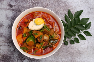 Flat lay of curry mutton noodle with curry leaves insight.