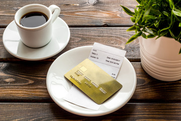 Paying in restaurant. Bank card near cup of coffee on dark wooden table