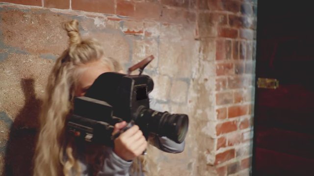 Young female video operator holding black cine camera camcoder. Teenage girl cinematographer standing near brick wall and shooting video with camera