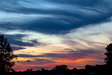 Picturesque landscape overlooking a red-orange sky with clouds and clouds at sunset at blue hour before the rain. Wallpaper and background with the concept of freshness and naturalness.
