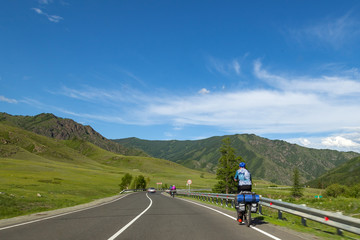 A strong man in helmet ride on sport bicycle with bags on a road in the mountains of the Altai climbing up by highway in autumn indian summer. Travelling and trip around the world.