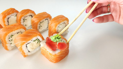 Hand with chopsticks takes the land. Hand takes the sushi with ginger and wasabi with chopsticks