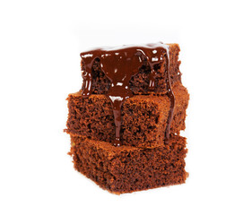Pieces of traditional Belgian chocolate biscuit brownie lies pyramid, poured melted warm chocolate, on a white background.